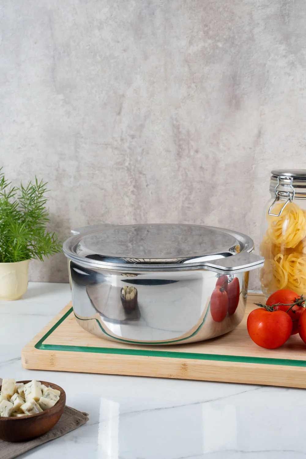 Una cacerola Essen con tapa sobre una tabla, con tomates y fideos al lado