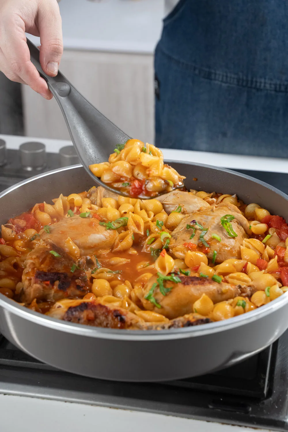 Una cuchara de silicona sirve fideos con pollo de una sartén Essen sobre la hornalla